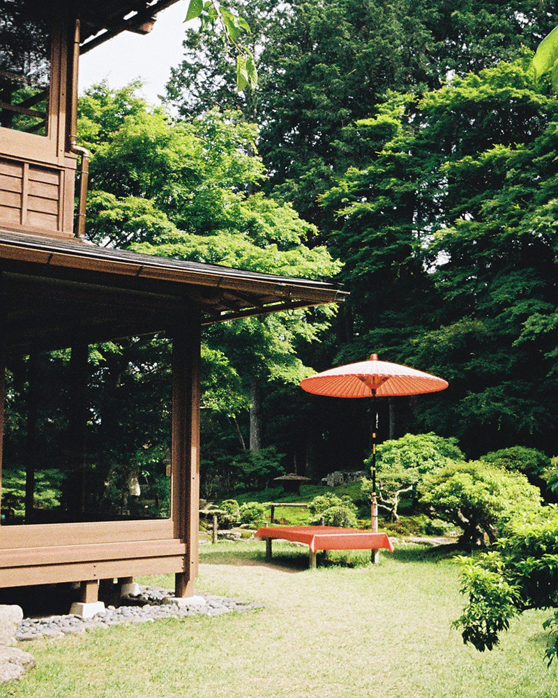旧竹林院の中の建物と赤い傘と赤い椅子。その後ろには庭園が広がっている。