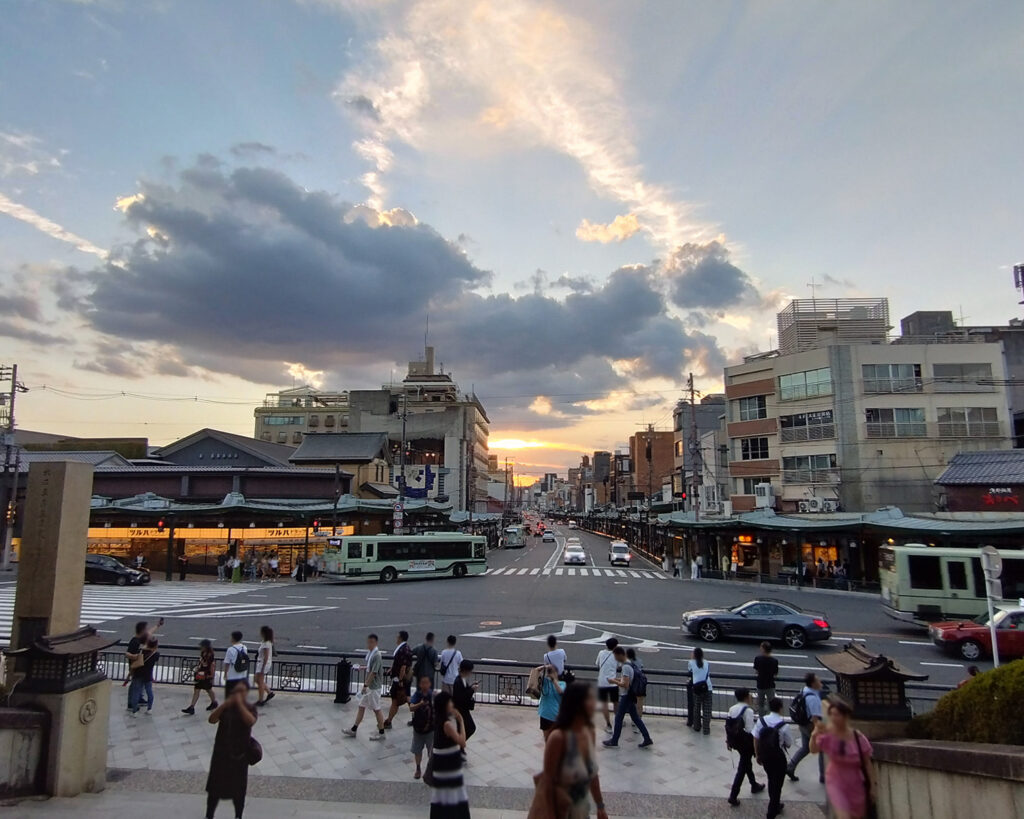 西楼門の内側から四条大橋の方を向いたときの夕焼け。建物の少し上に明るいオレンジのエリアがあり、その上にぶ厚めの雲がすこし、その上は空が広がっている。