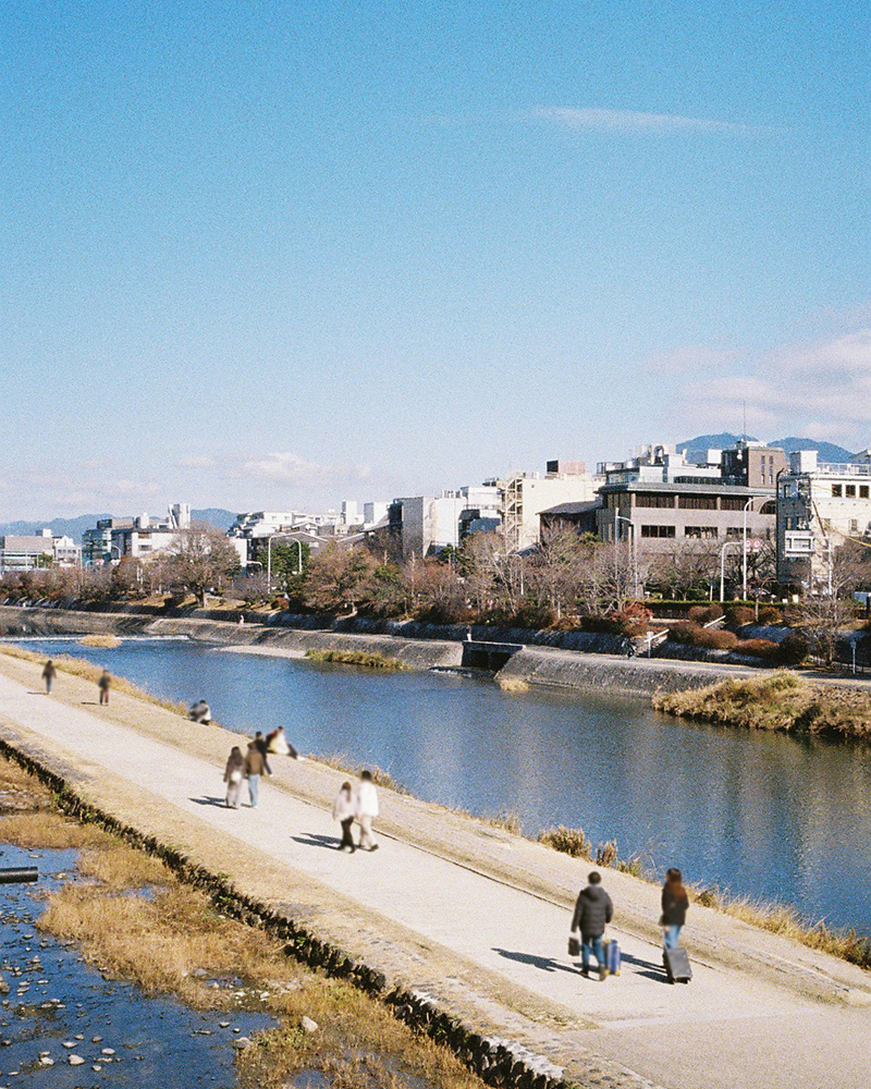 橋のはしっこから撮った川と空。河川敷は人が散歩している。